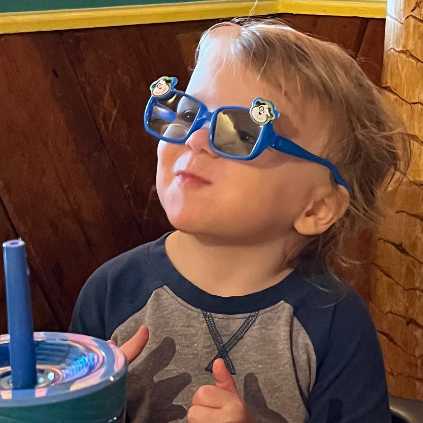 A young boy wearing sunglasses at a table.