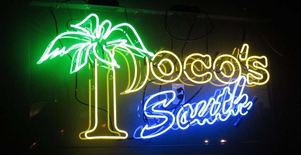 A neon sign that says doco's beach.