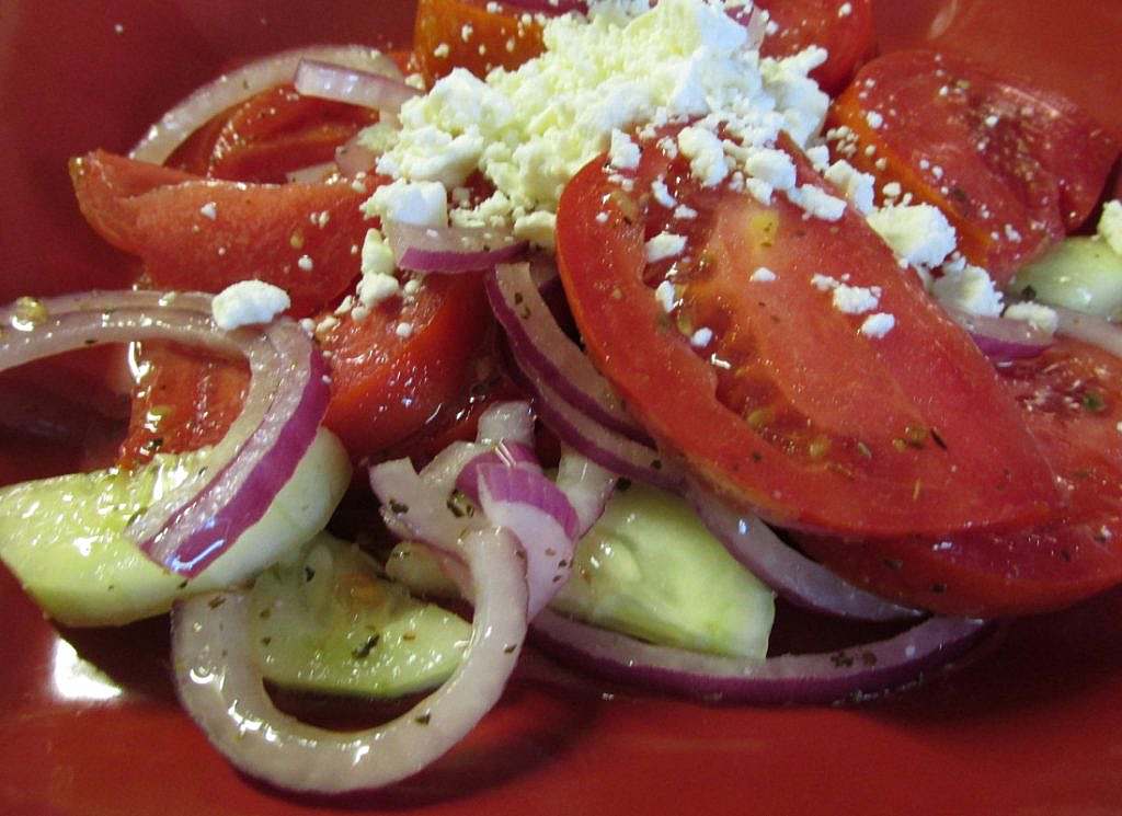A red plate with tomatoes, cucumbers, onions and feta cheese.