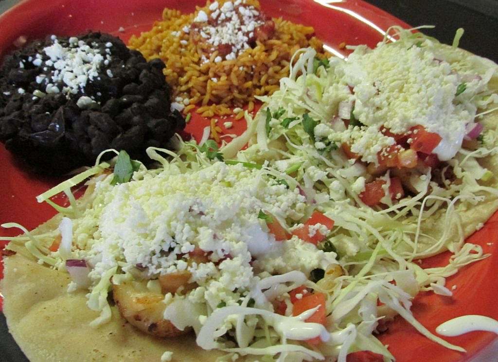 Three tacos on a red plate with rice and black beans.